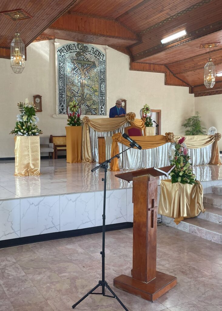 In a simple church, a pastor in a suit stands at the alter.