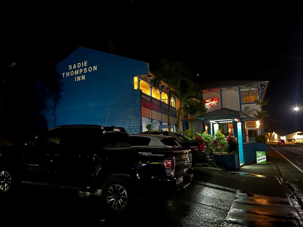 At night, a large two story building looms over a parking lot, with the glow of yellow lights reflected off the rain-soaked streets.