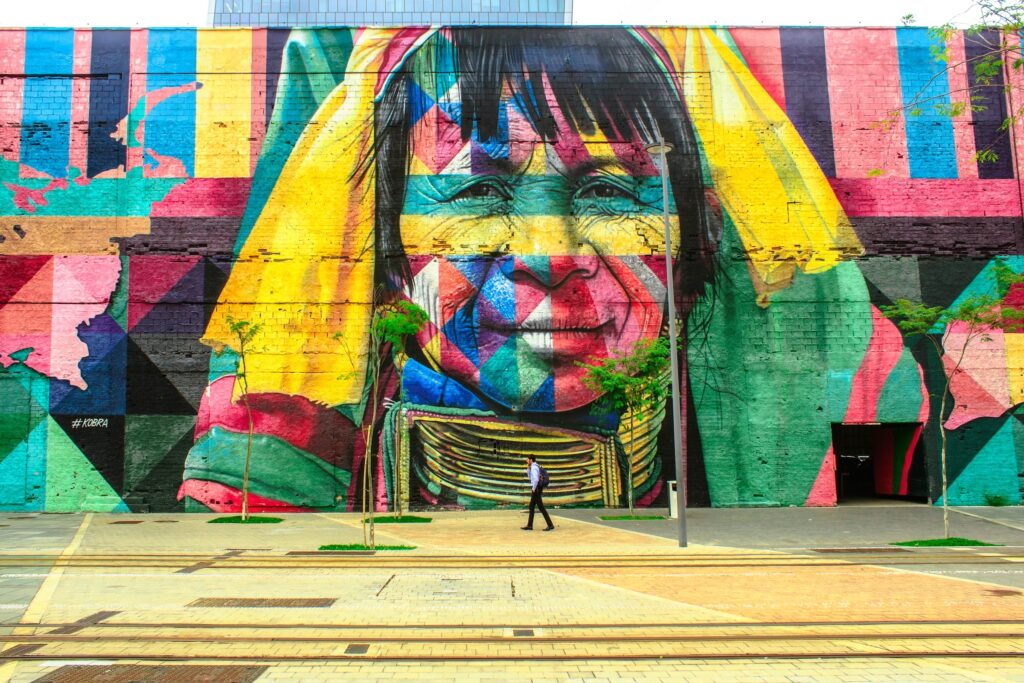 A bright multi-colored mural against a large wall depicts an older woman in a headscarf, while a man in business attire walks by.