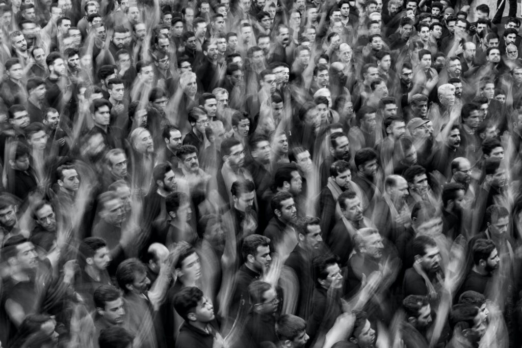A layered image shows a large crowd of men waving their hands in the air.