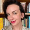 A woman with red lipstick smiles in front of a book shelf.