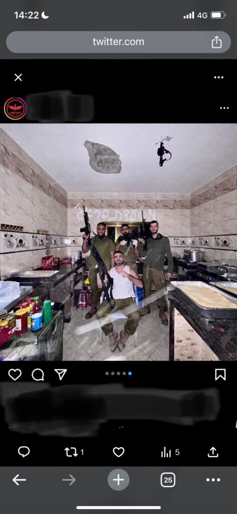 An image from a cellphone shows a photo of four men holding guns and wearing green army fatigues and boots inside a kitchen with food items atop tables.