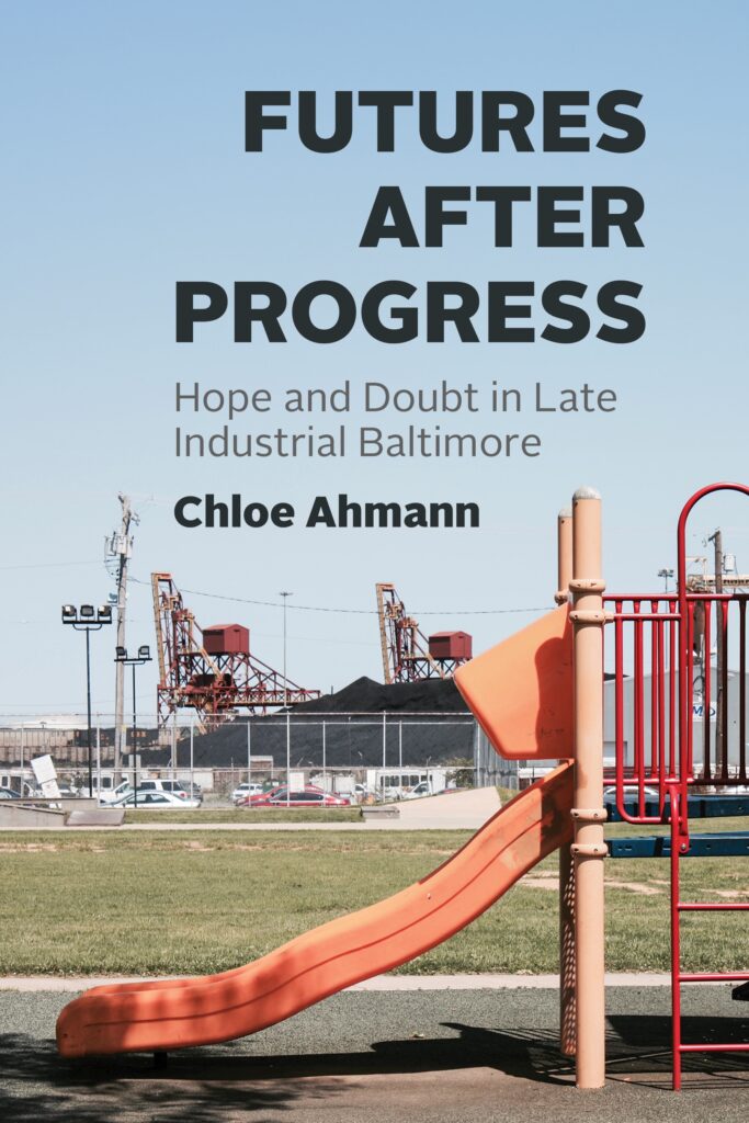 A book cover shows a red-and-orange playground slide in the foreground and factory buildings and machinery behind a fence in the background. Above the image, text reads “Futures after Progress: Hope and Doubt in Late Industrial Baltimore” and “Chloe Ahmann.”