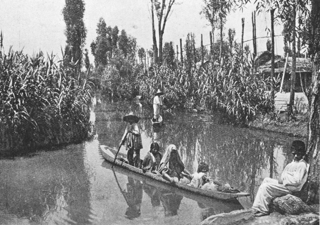 A black-and-white photo shows several people floating in a canoe between shores lined with high grasses.
