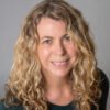 A woman with blond curly hair smiles at the camera.