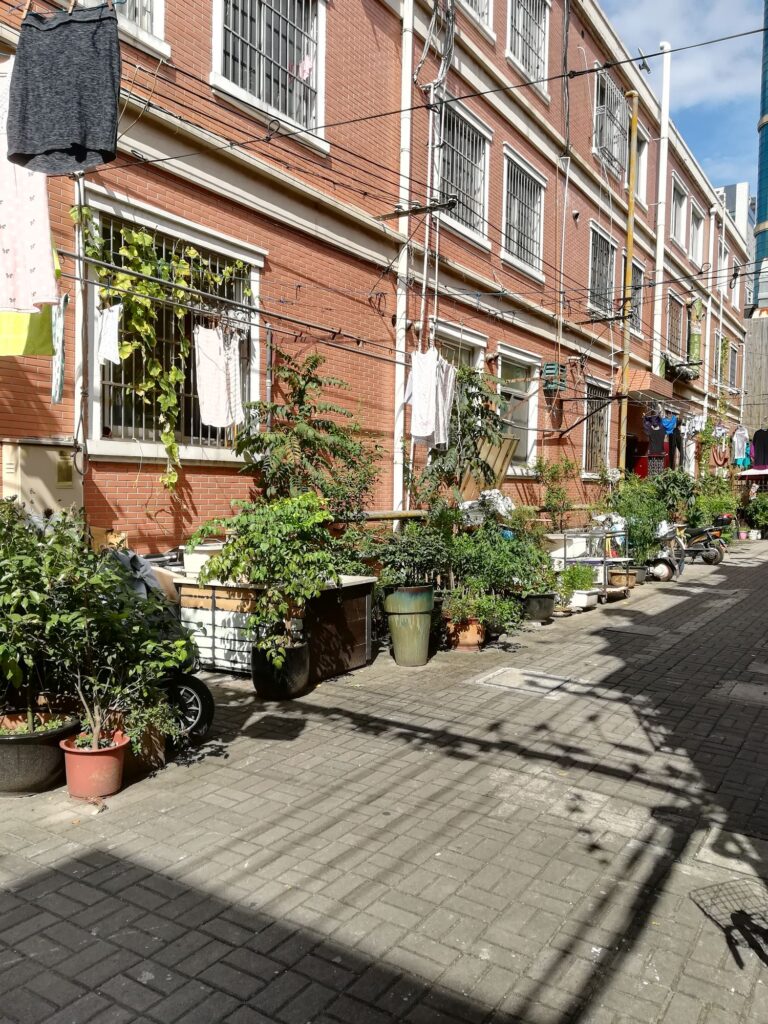 Numerous potted plants grow outside a three-story brick housing complex.