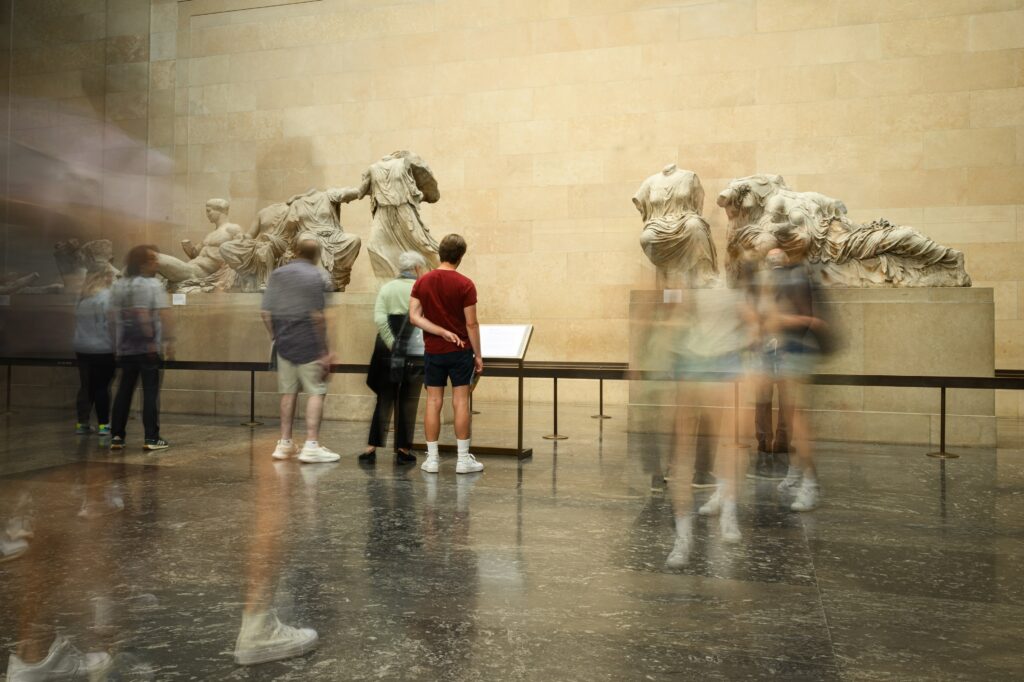 Blurred people move through a museum gallery where ancient statues are displayed.