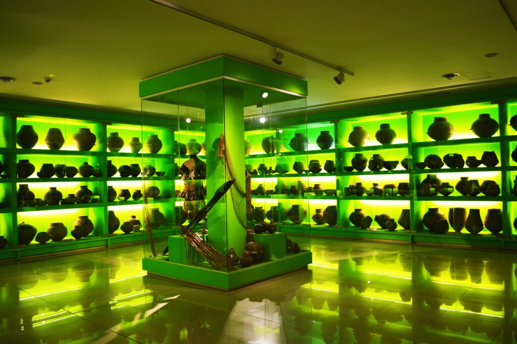 Shelves backlit with glowing green lights display rows of ancient artifacts.