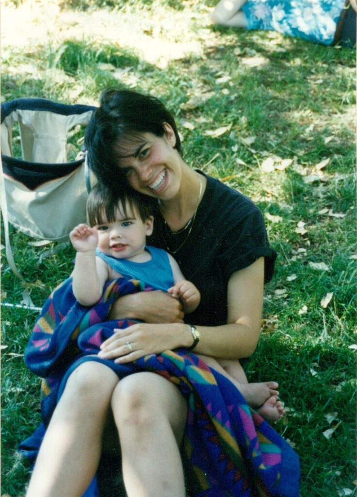 A smiling woman sits on the grass holding a happy child on her lap.James McCanna