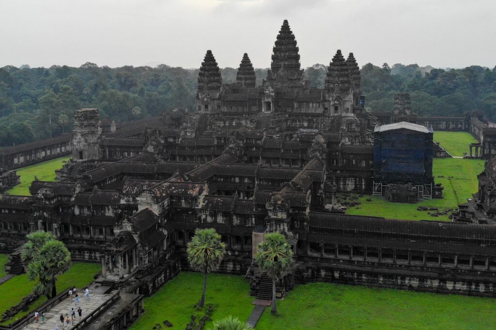 A compound of buildings that are covered in black crusts is surrounded by vibrant green grass and trees.