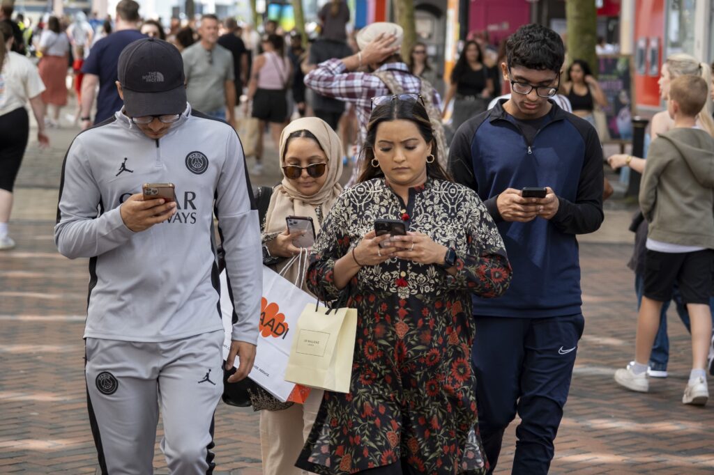 People walking down a busy pedestrian street look down at their smartphones.