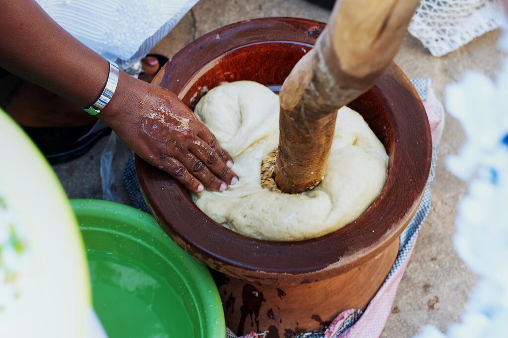 With their right hand, a person reaches into a reddish clay vessel that contains a soft white substance, out of which a large stick emerges.