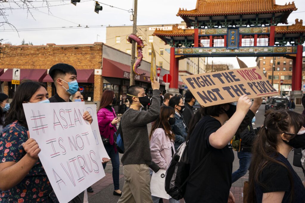 Demonstrators in surgical masks march through a city’s streets displaying signs that read “Fight the virus not the people” and “Asian is not a virus.”