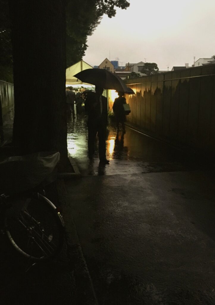 Two people walk beside a wall on a narrow street holding umbrellas.