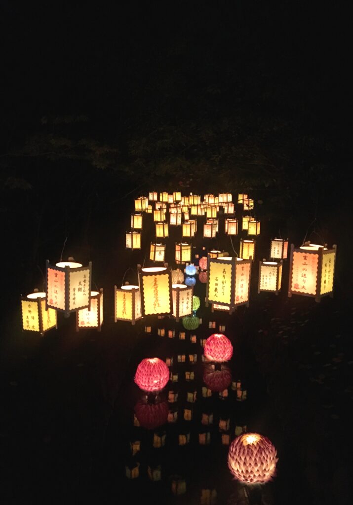 Cubic and spherical lanterns, some with Japanese characters on them, glow in the darkness.