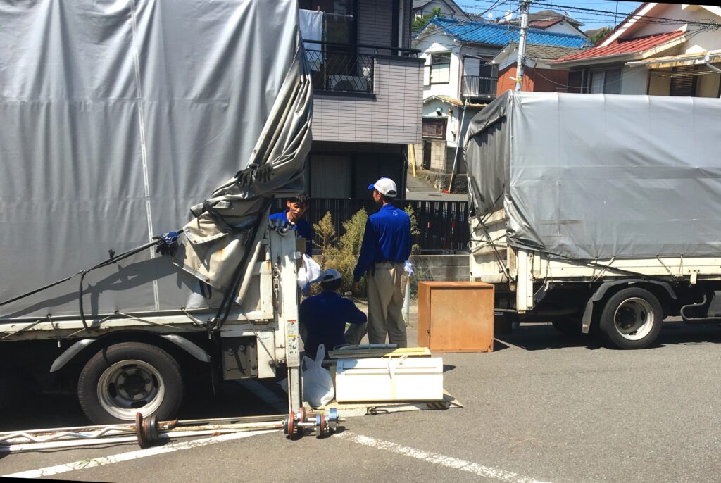 A few people unload two trucks in a parking lot.