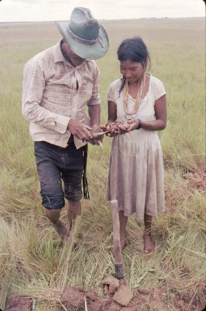 Two people stand together in a wide open grassy plain.