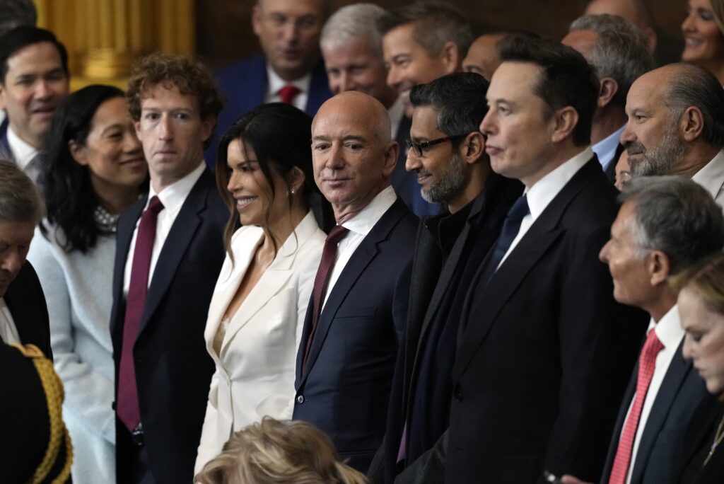 A row of formally attired people noted for their wealth and power stands together looking smug.