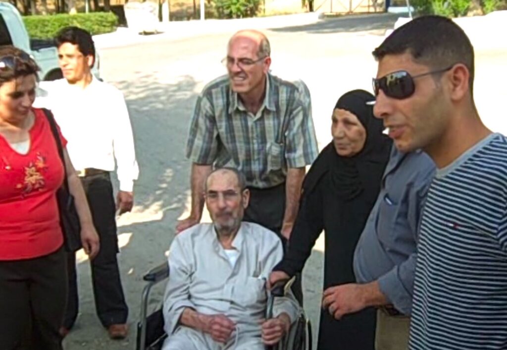 A man in a wheelchair is surrounded by six people in red, white, plaid, black, and striped clothing.
