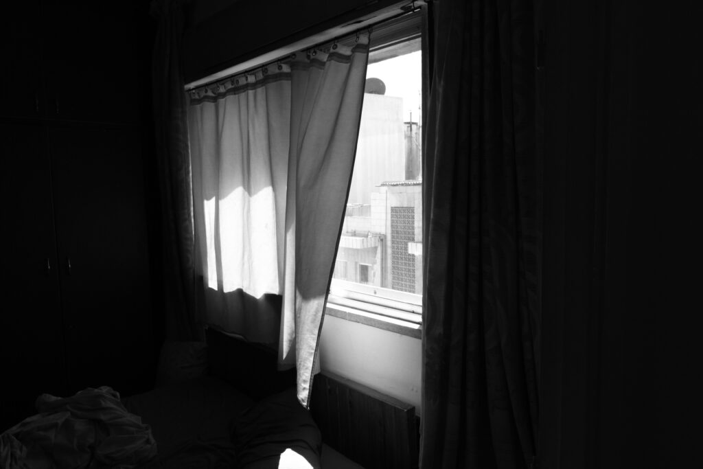 A black-and-white image features a window with the curtain pushed open by a soft breeze.