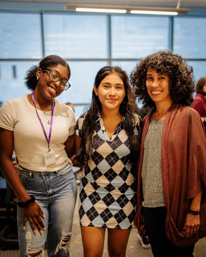 Three people smile with their arms around one another.