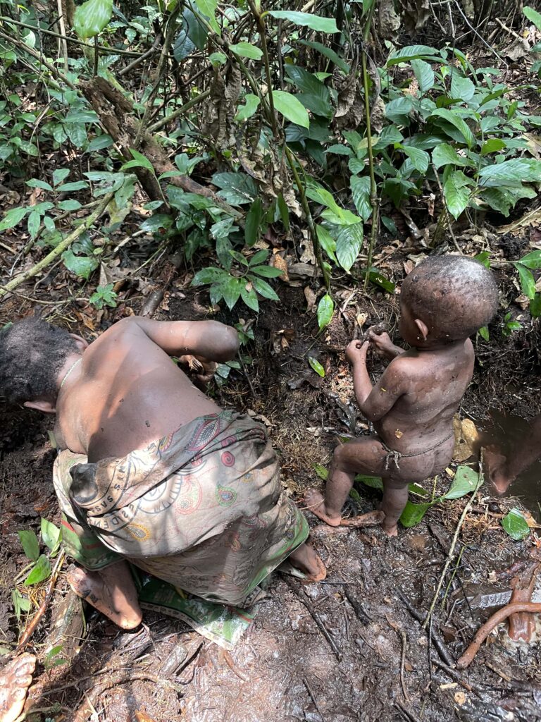 Two small children fish amid dense trees and brush.