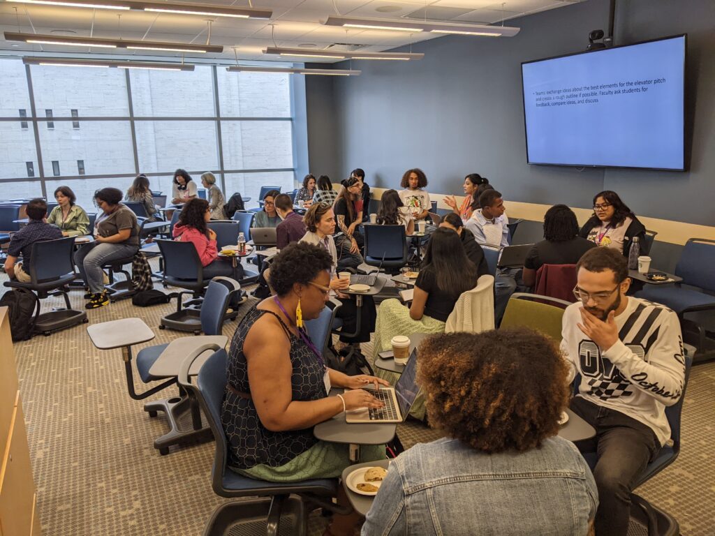 Small groups of people sit working together in clusters in a classroom.