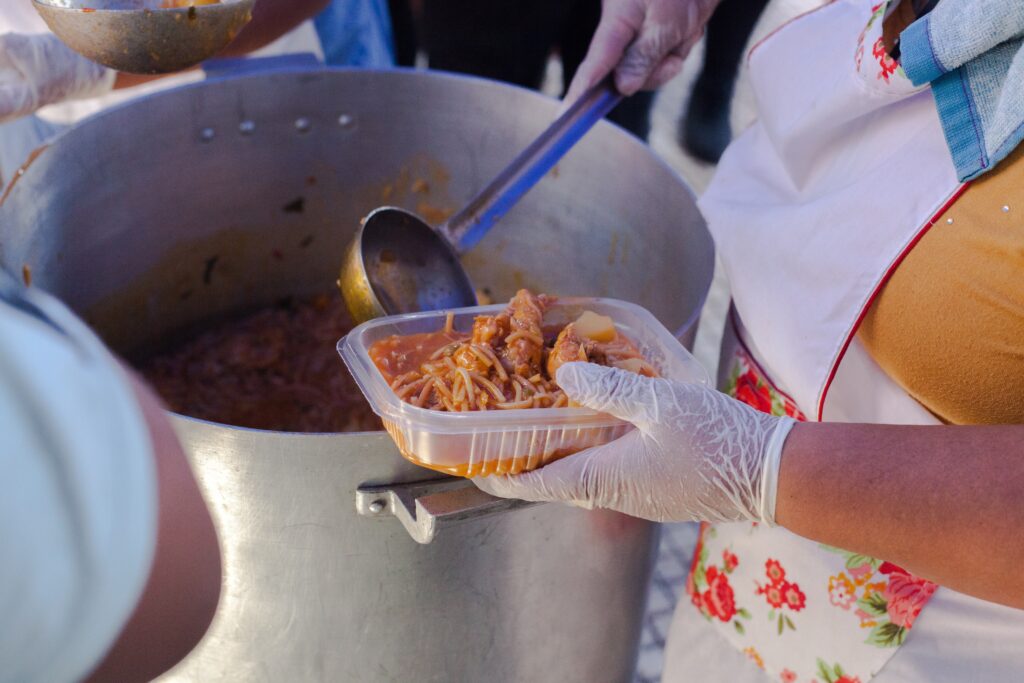 A person ladles stew out of a large pot into a plastic container.