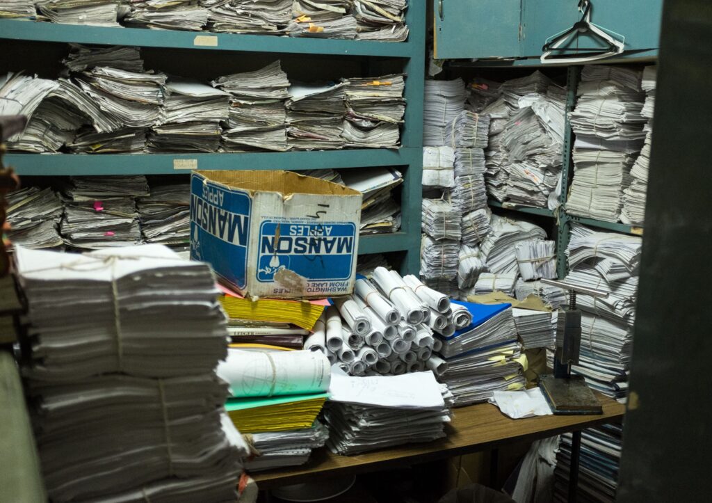 In a small room, stacks and rolls of papers fill teal-colored shelves and cover a table.