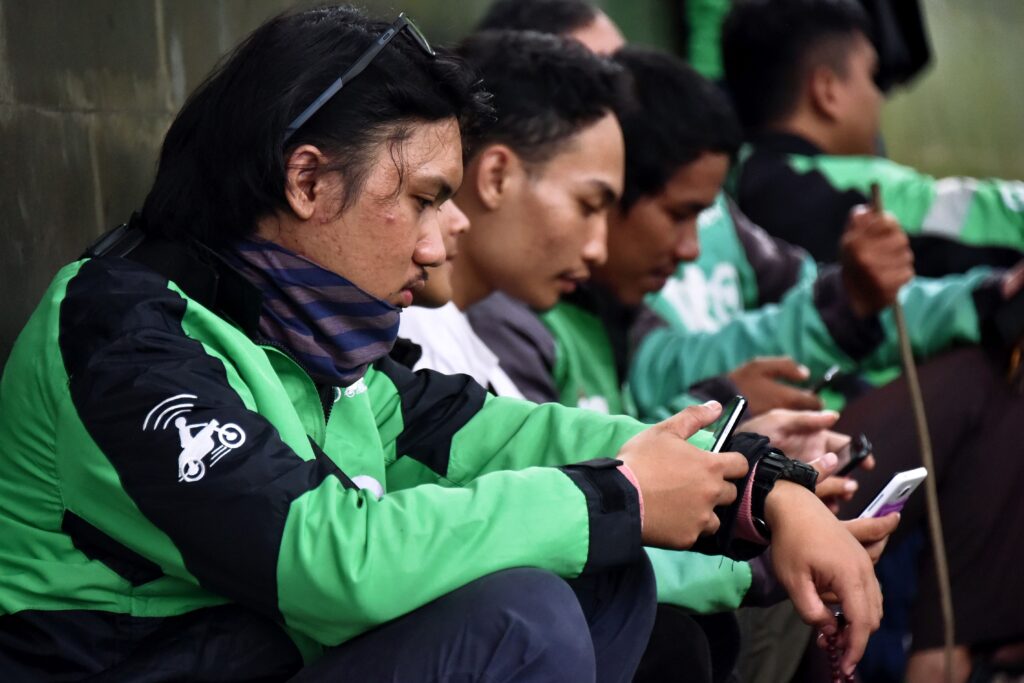 People wearing green and black jackets with motorbike symbols on them sit and look at their mobile phones.