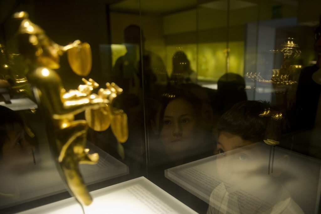 Luzes e rostos são refletidos em uma vitrine de vidro que contém uma estatueta de ouro.