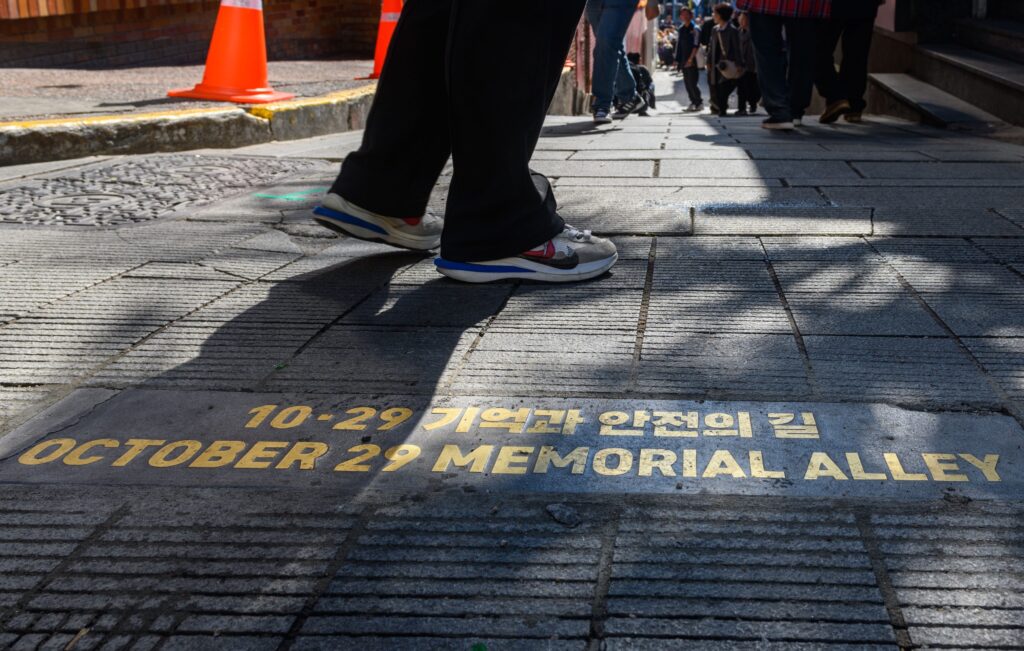 A closeup in yellow block letters in Korean and English reads “October 29 Memorial Alley” on a dark-gray, concrete walkway.