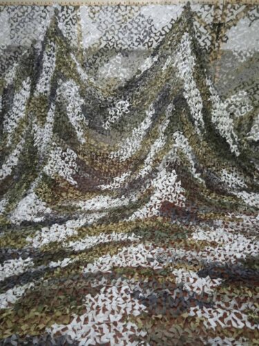 A large, loosely woven net of mottled white, brown, black, and green colors is draped on a loom and ripples profusely onto the floor.