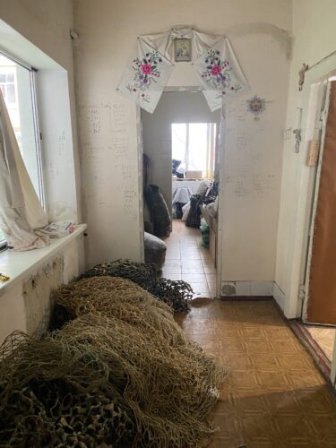 Large piles of olive-green netting lie beneath a window in the hallway of an apartment.