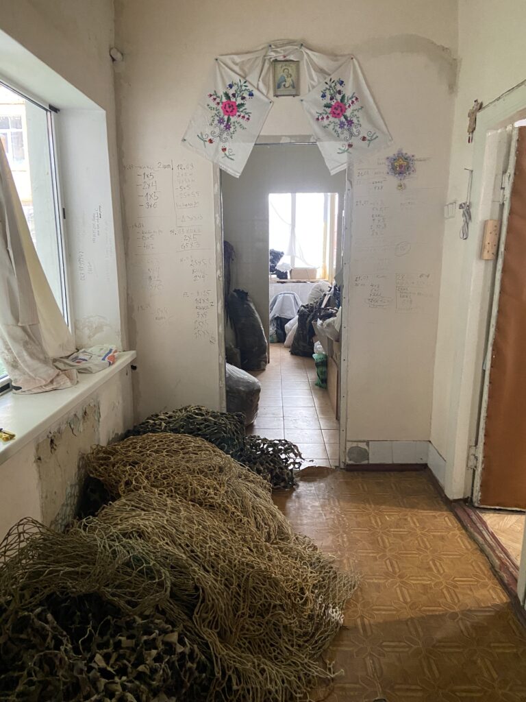 Large piles of olive-green netting lie beneath a window in the hallway of an apartment.