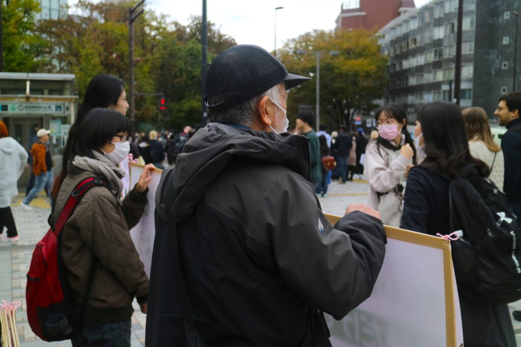 Two people shown from the back hold a sign up as several passersby stop to look.