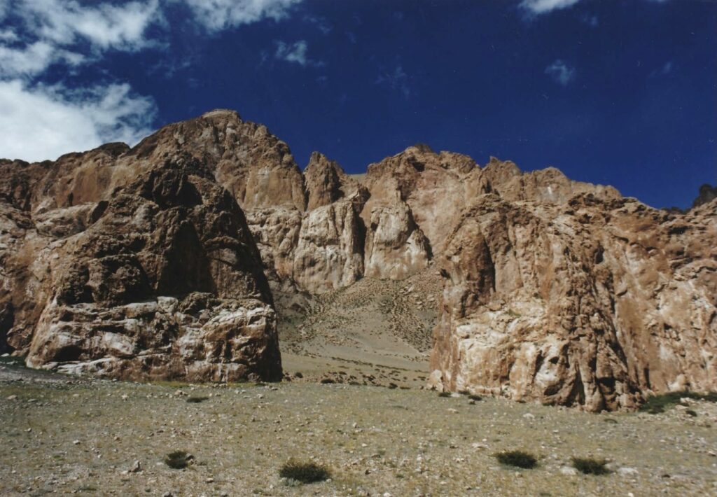 A reddish rocky ridge rises up beneath a blue sky with white clouds.