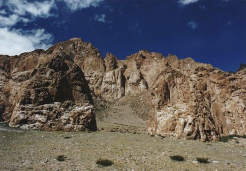 A reddish rocky ridge rises up beneath a blue sky with white clouds.